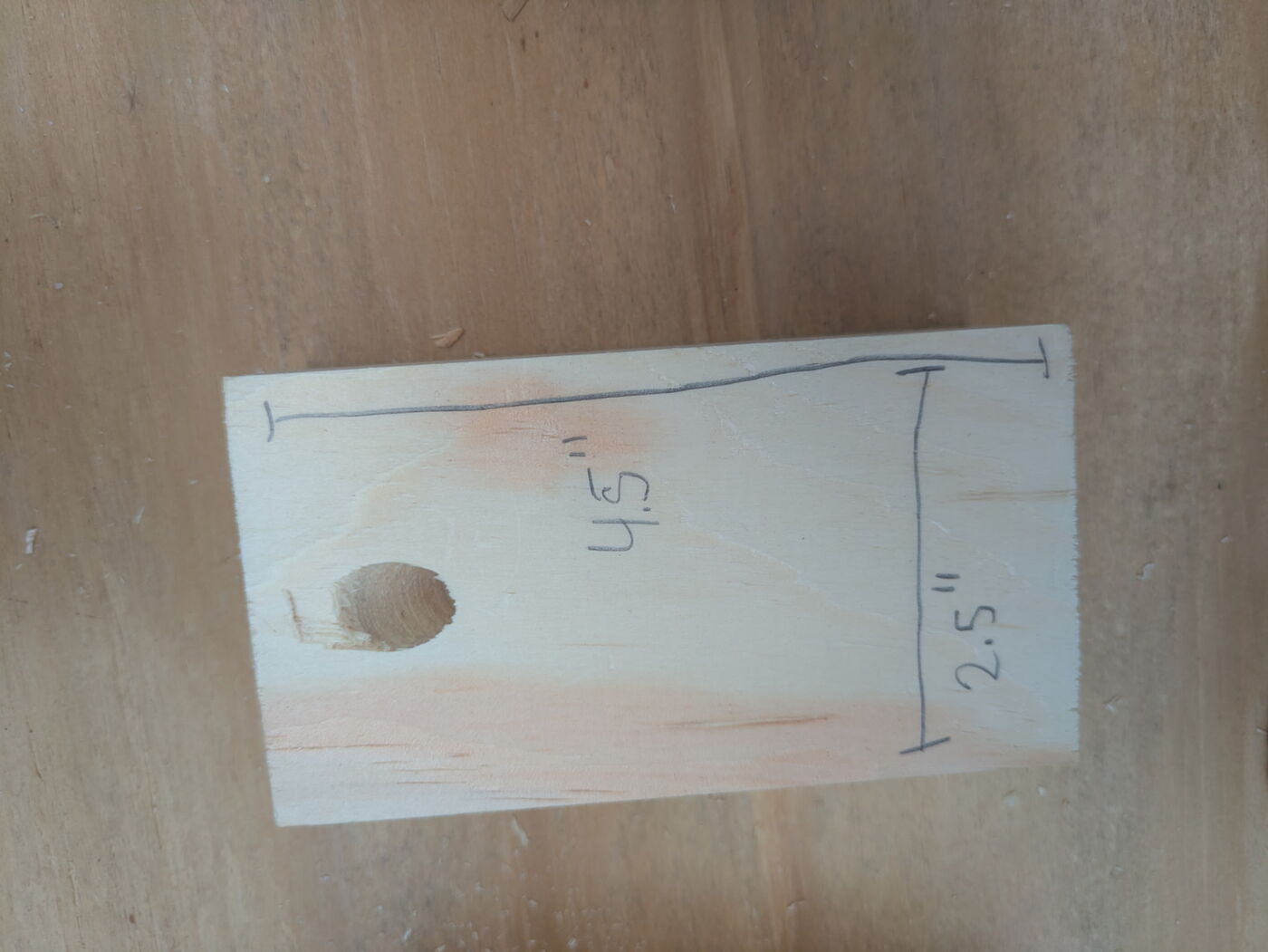 Close-up of a pine side piece with a drilled hole, marked 4.5 inches by 2.5 inches.