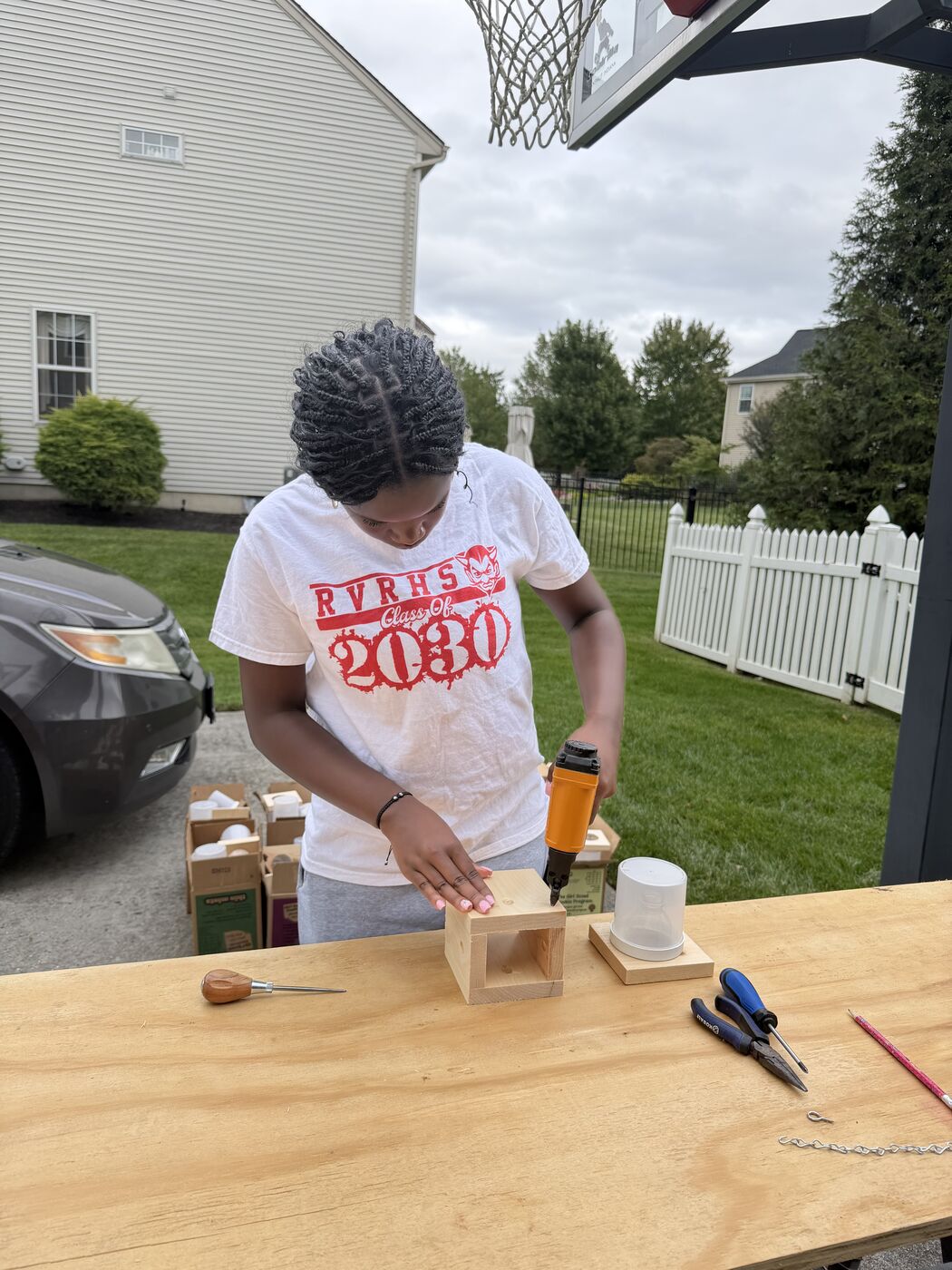 A troop member using a nail gun to assemble a pine box on a table.