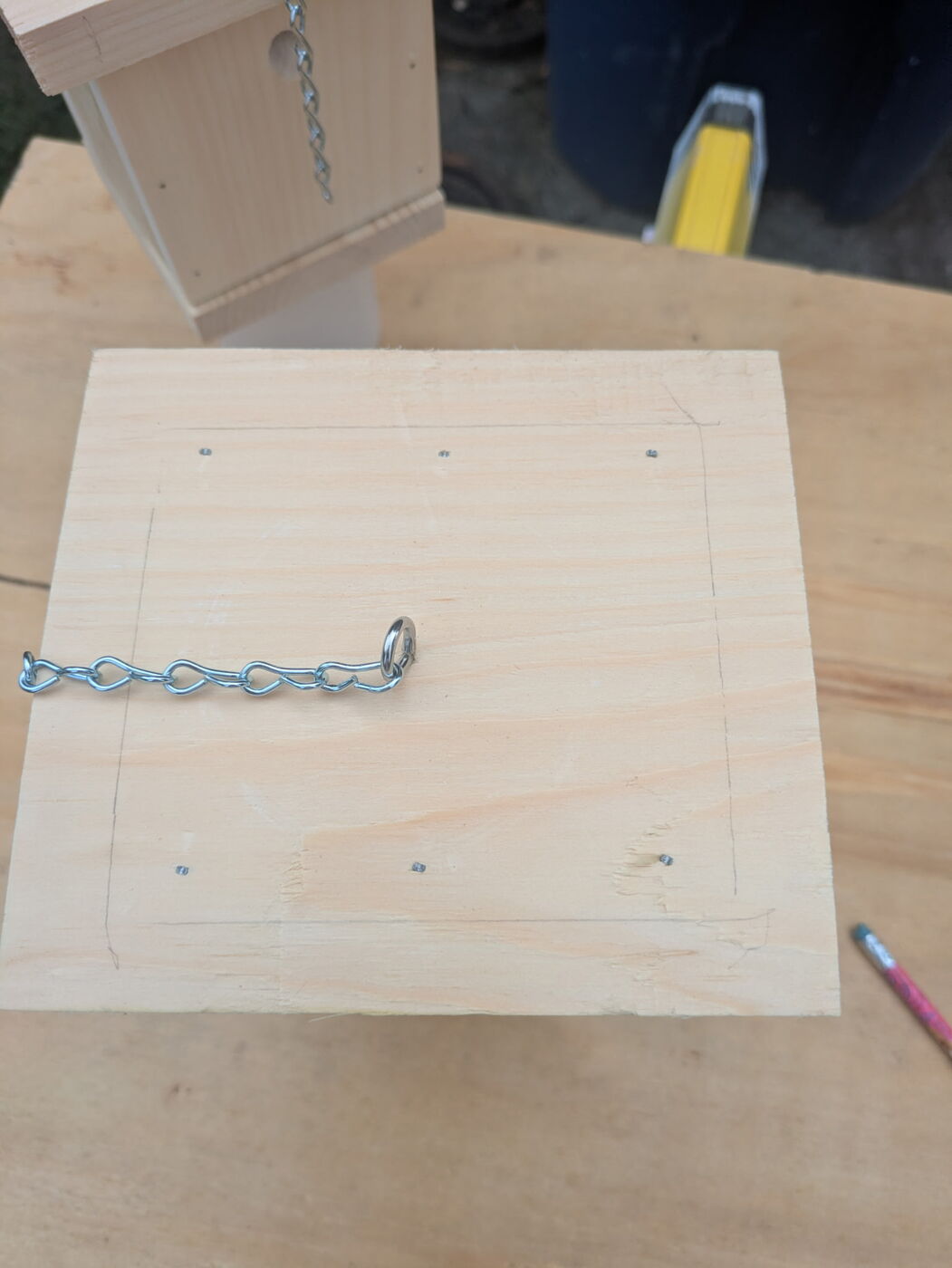 A completed pine bee trap hanging by its chain, with the entry hole in the side and a jar underneath.